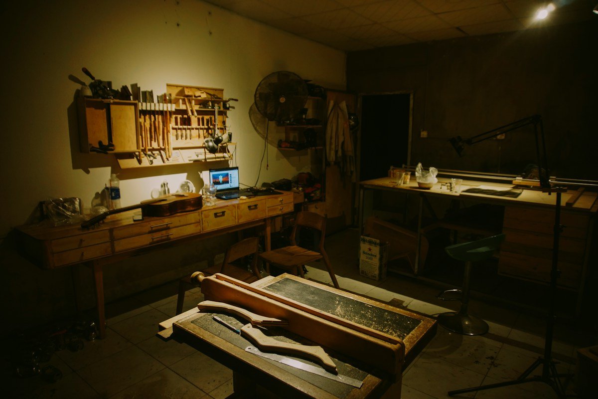 Un atelier sombre éclairé à la lampe, avec des outils accrochés au mur et un établi encombré